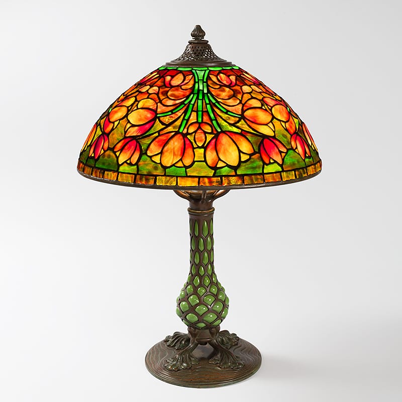 Stained glass table lamp with floral pattern and green base on white background.