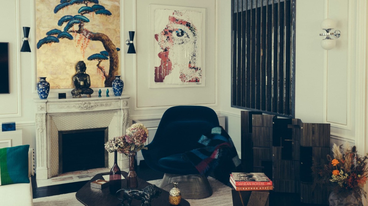 Modern living room with abstract art, a dark chair, a Buddha statue on a mantel, and decorative vases.