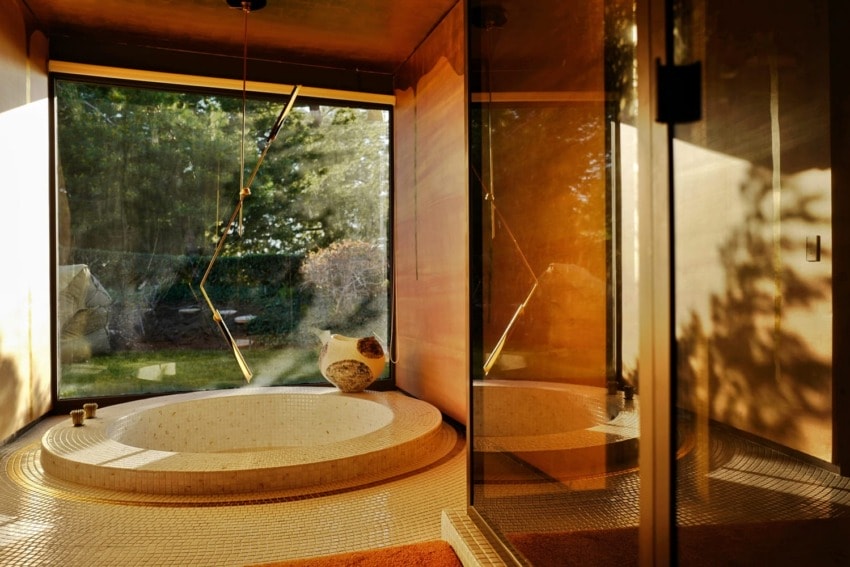 Luxurious modern bathroom with a large circular tub, floor-to-ceiling windows, and warm natural lighting.