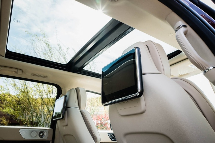 Rear seat entertainment screens and panoramic sunroof in a luxury vehicle interior with beige upholstery.