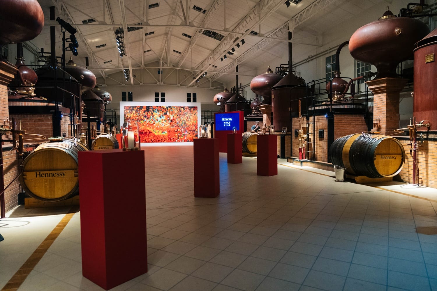 Distillery interior with large barrels, copper stills, and colorful artwork on the wall in a well-lit room.