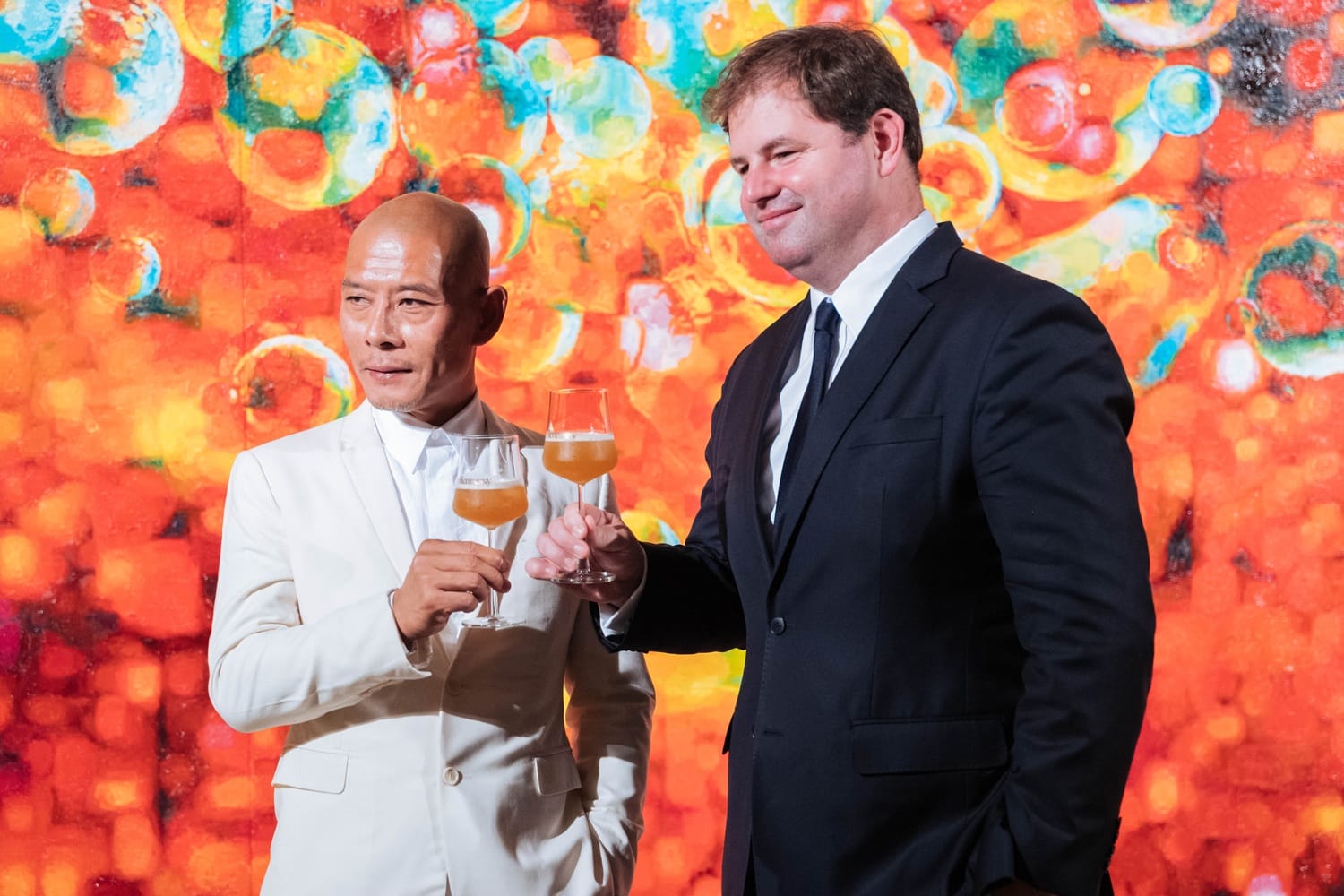 Two men in suits toasting with glasses against a vibrant, colorful background.