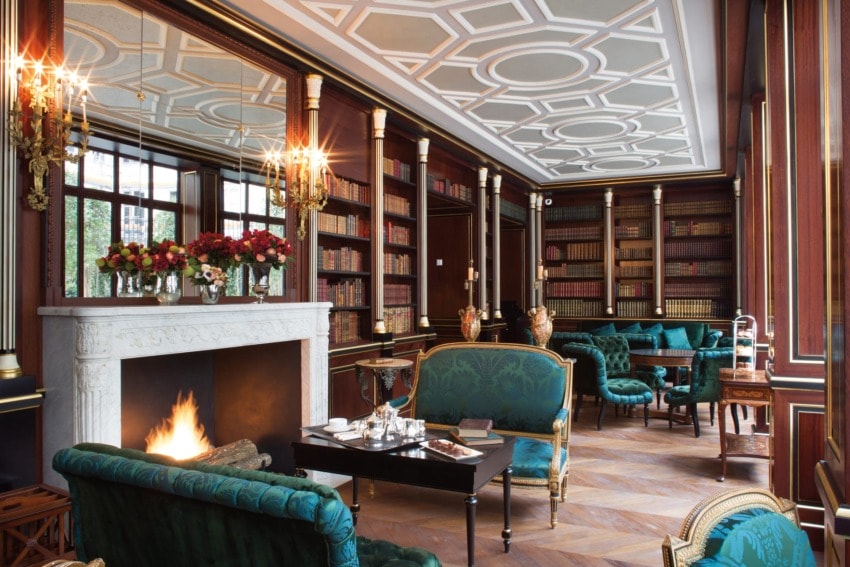 Luxurious library with a lit fireplace, elegant green sofas, and shelves filled with books.