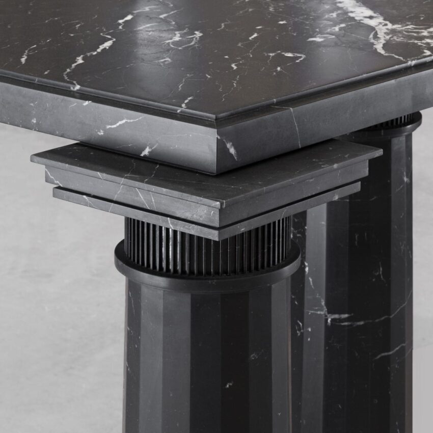 Close-up of a black marble table with detailed veining, featuring sturdy pillar-like legs and geometric design elements.