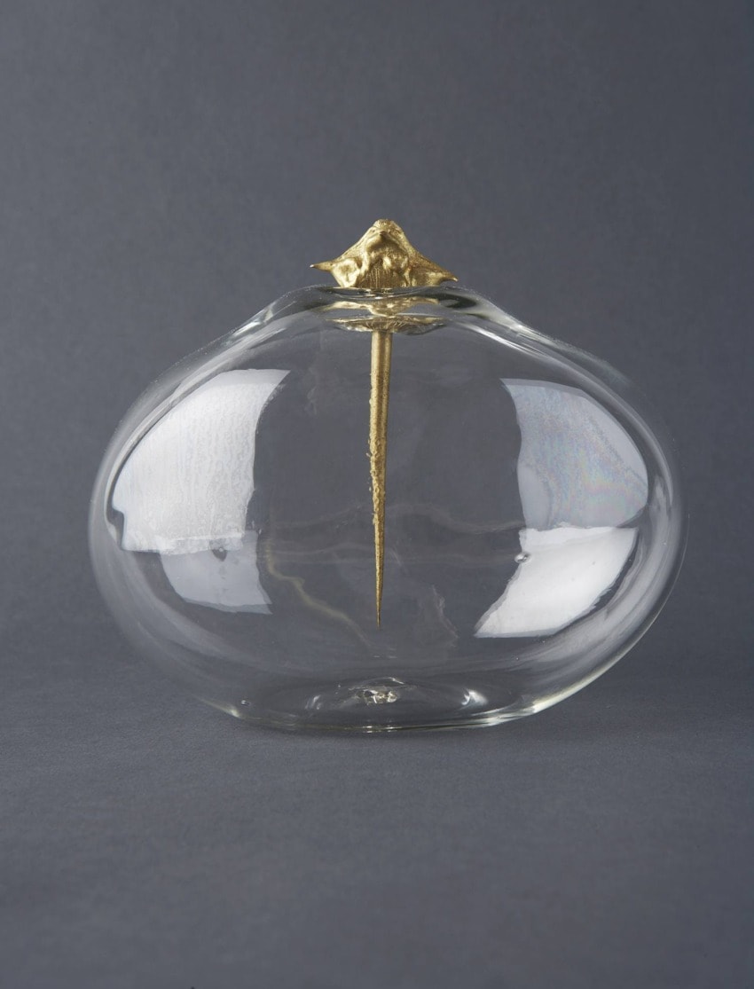 A glass vessel with a gold decorative element at the top, set against a dark gray background.