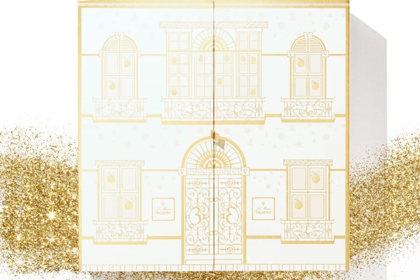 Gold-trimmed elegant gift box with decorative building facade design, surrounded by shimmering gold glitter.