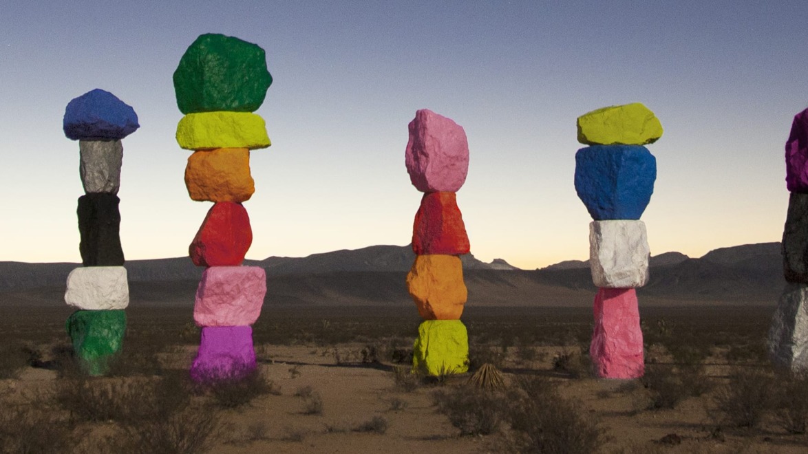 Colorful rock sculptures standing in the desert against a mountain backdrop at dusk.