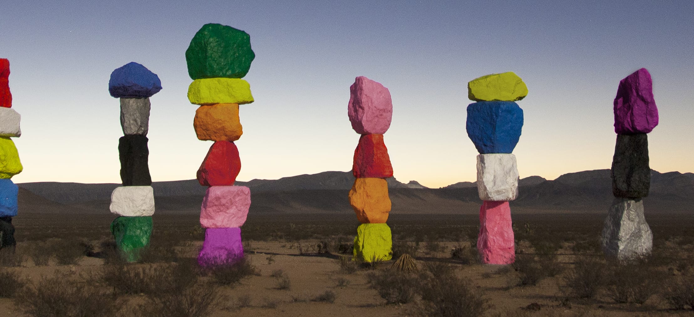 Colorful rock sculptures standing in the desert against a mountain backdrop at dusk.