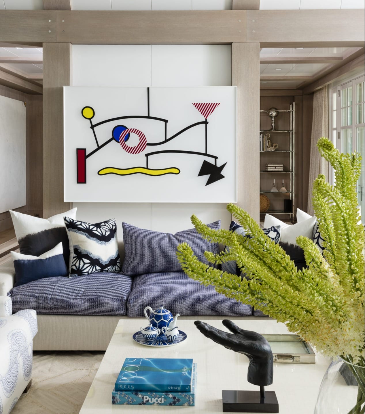 Modern living room with abstract wall art, blue and white cushions on gray sofa, and decorative books and sculpture on table