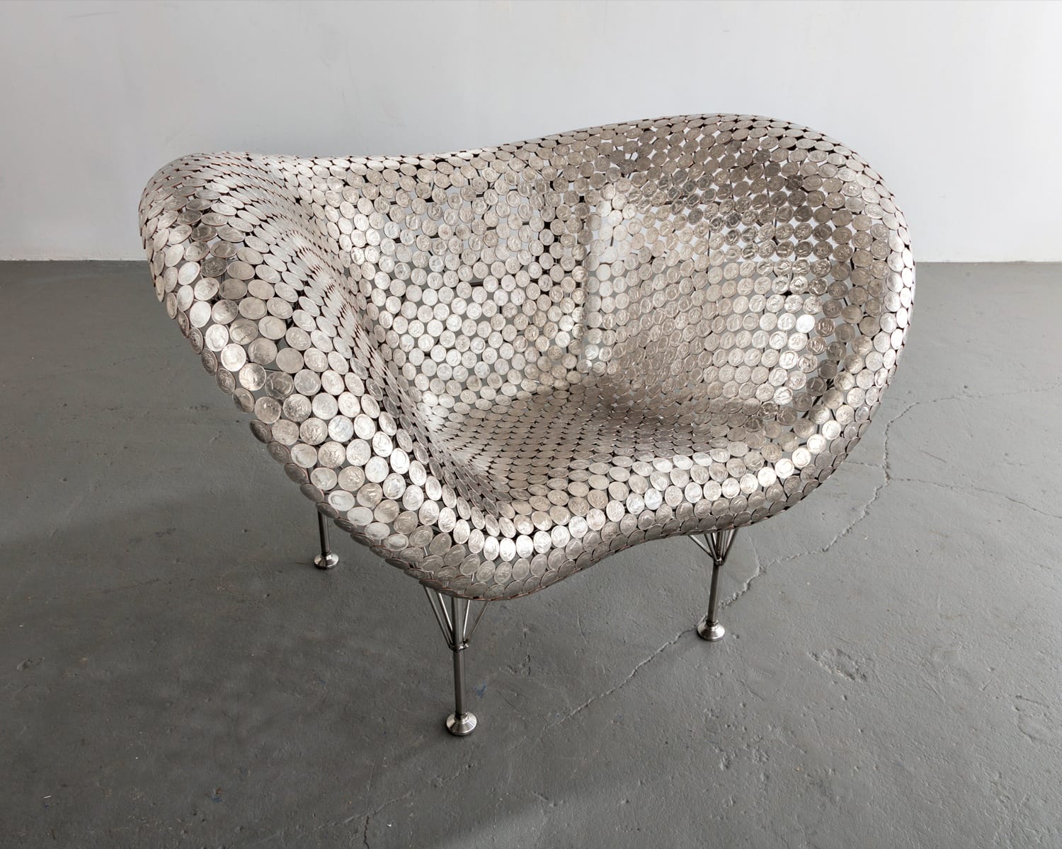 Futuristic chair made of metal discs, featuring a curved design and thin metallic legs on a gray floor background.