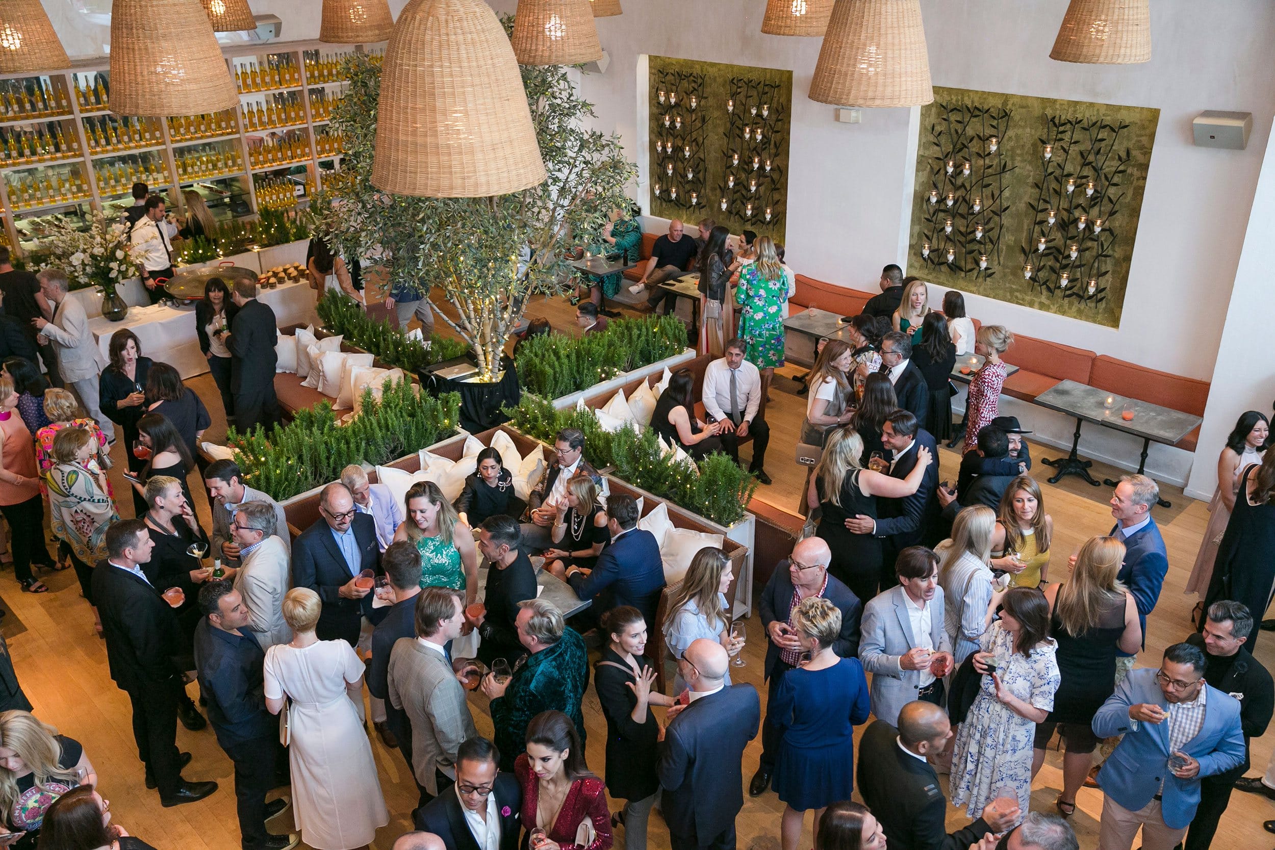 A lively, elegant social gathering in a stylish restaurant with people mingling and enjoying drinks.