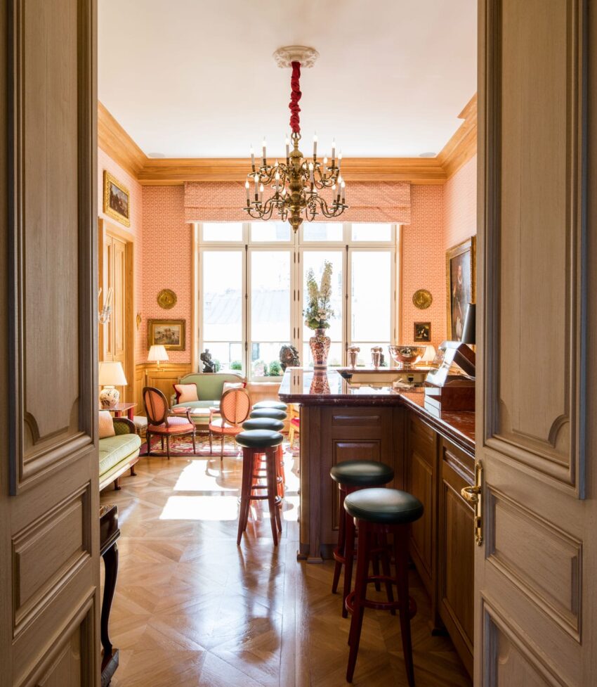 Elegant living room with wooden floors, chandelier, bar stools, large window, and classic decor.
