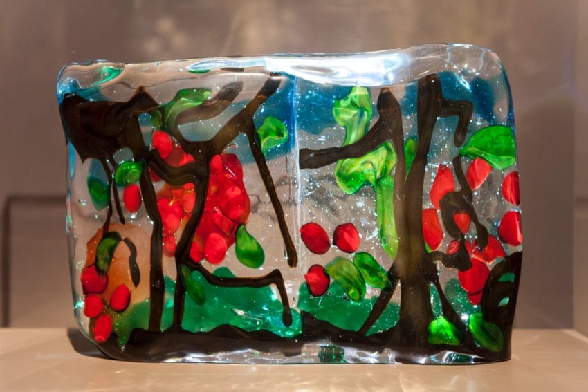 Colorful abstract glass sculpture with red, green, and black patterns on a blue background.
