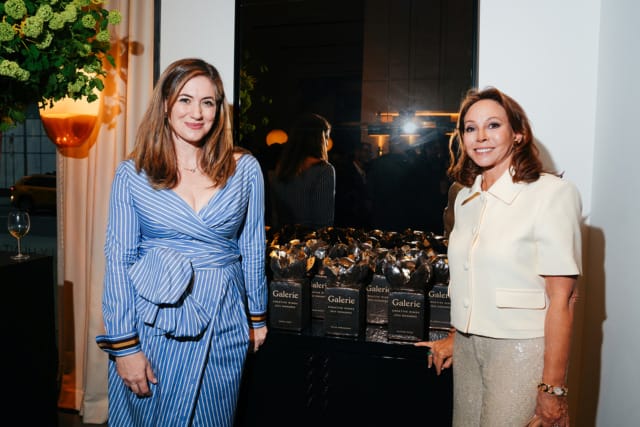 Two women posing near a table with gift bags in a stylish indoor setting.