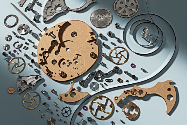 Disassembled watch parts including gears and screws arranged on a blue surface, showcasing intricate mechanisms.