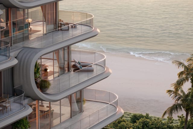 Luxury beachfront apartments with curved balconies overlooking the ocean and sandy beach at sunset.
