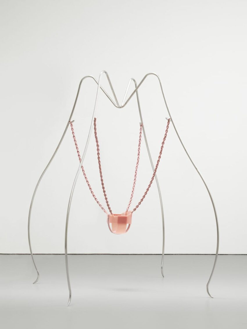 Modern sculpture with thin metal wires forming a structure holding a pink translucent element in the center against a white background.