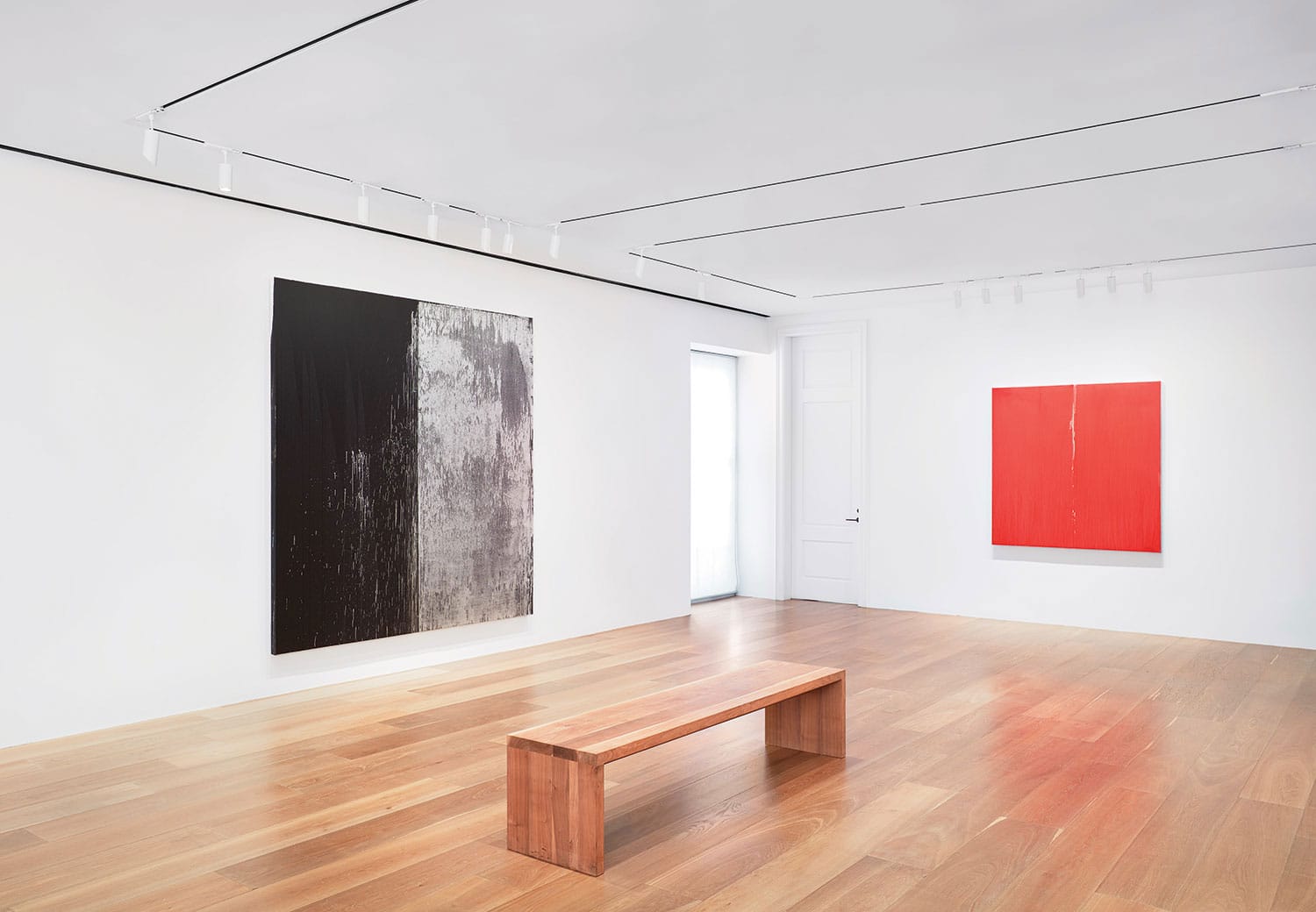 Gallery interior with wooden bench, two abstract paintings on white walls, and light wooden flooring.
