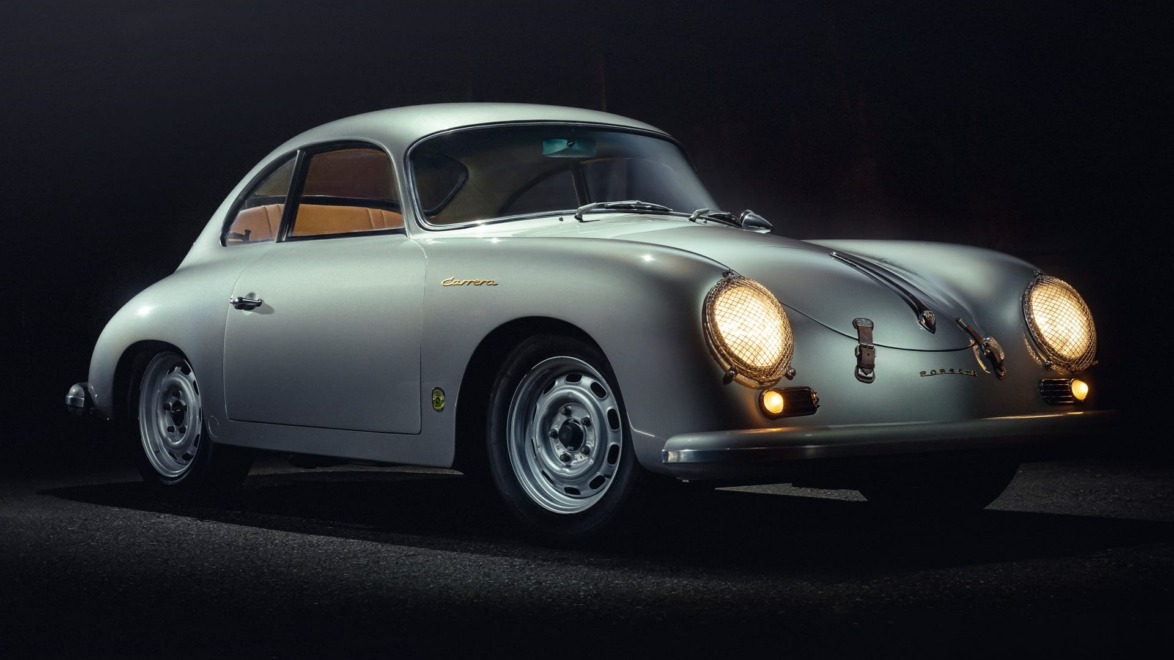 Vintage silver sports car with rounded design, illuminated headlights, and classic wheels parked on a dark road background.