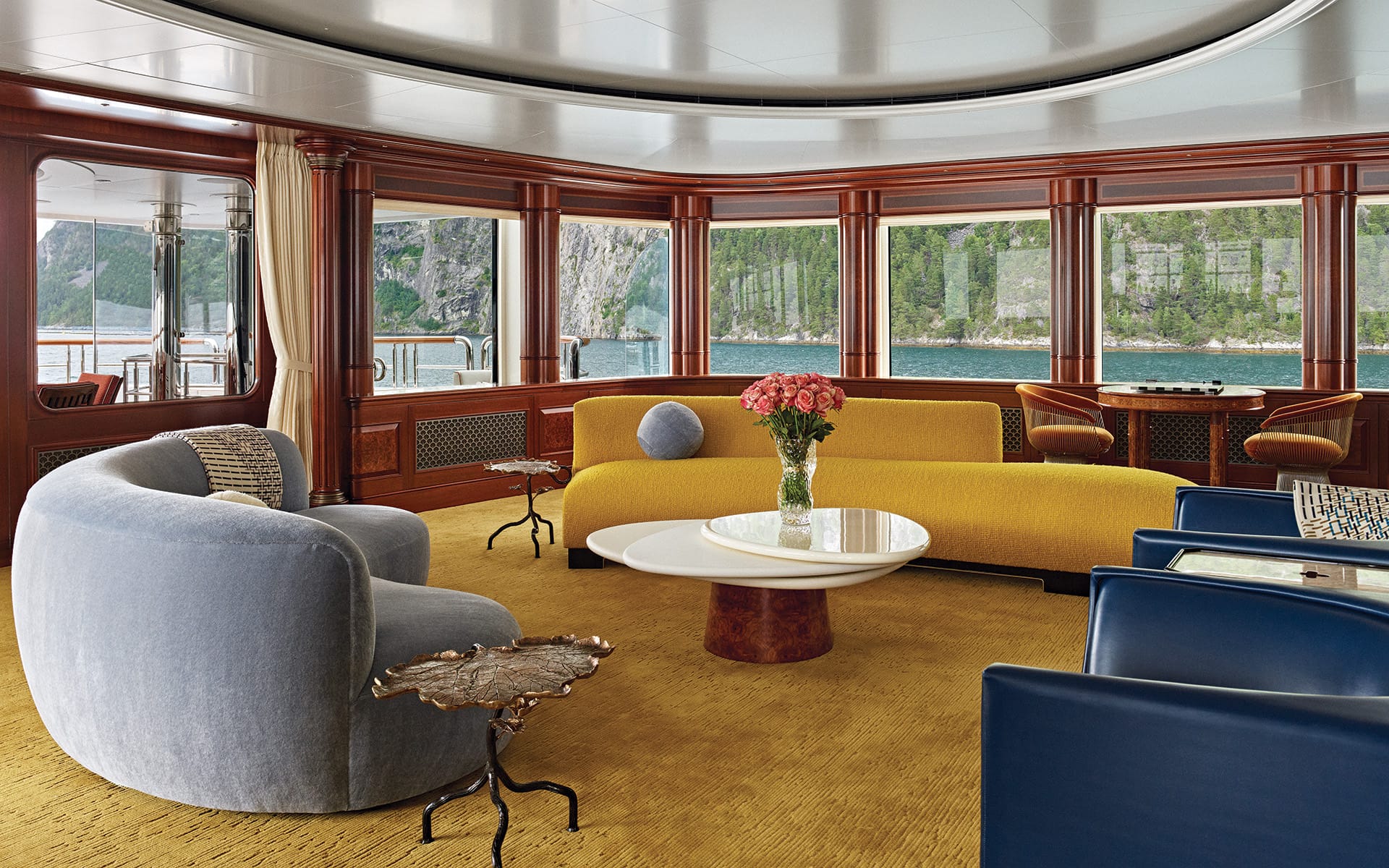 Luxurious yacht interior with modern seating, round table, and ocean view through large windows.