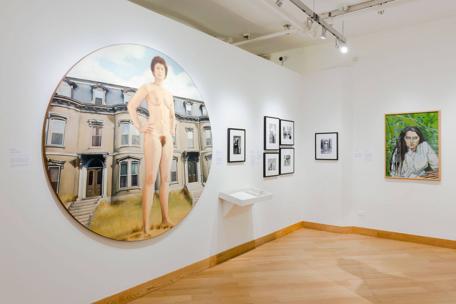 Art gallery with paintings and photographs displayed on white walls and a wooden floor.