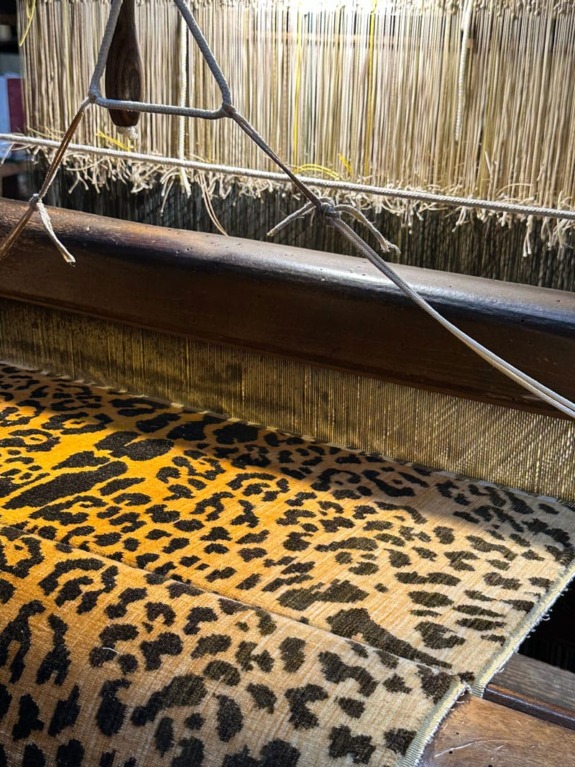 Traditional loom weaving leopard pattern fabric under warm light.