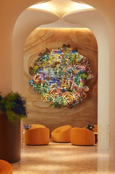 Abstract colorful art installation on curved wood wall, with orange chairs and potted flowers in a modern, cozy room.