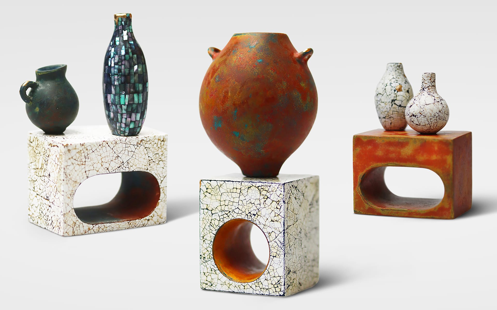 Various textured and patterned pottery vases displayed on modern geometric stands with a white background.