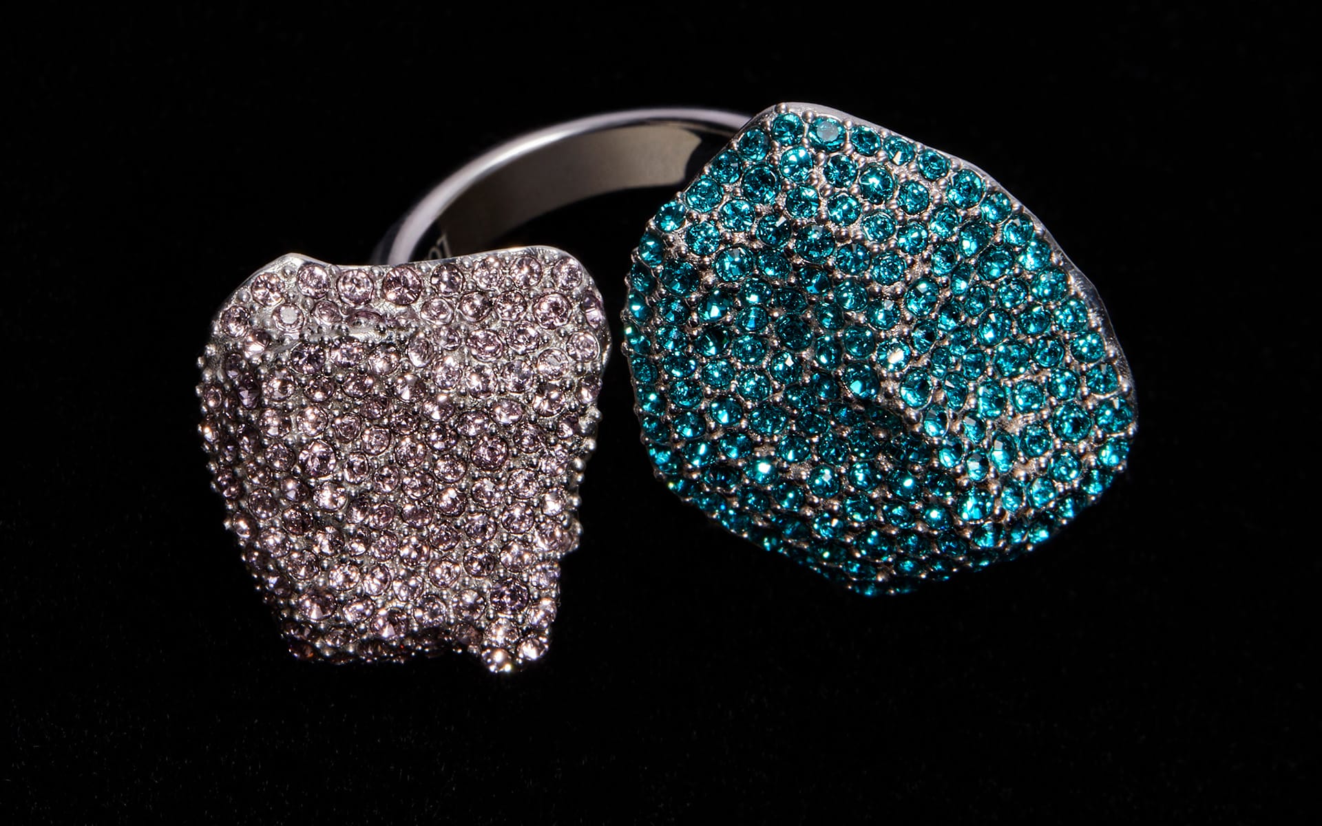 Silver ring with two textured stones, one covered in small clear gems and the other in sparkling turquoise gems, on a black background.