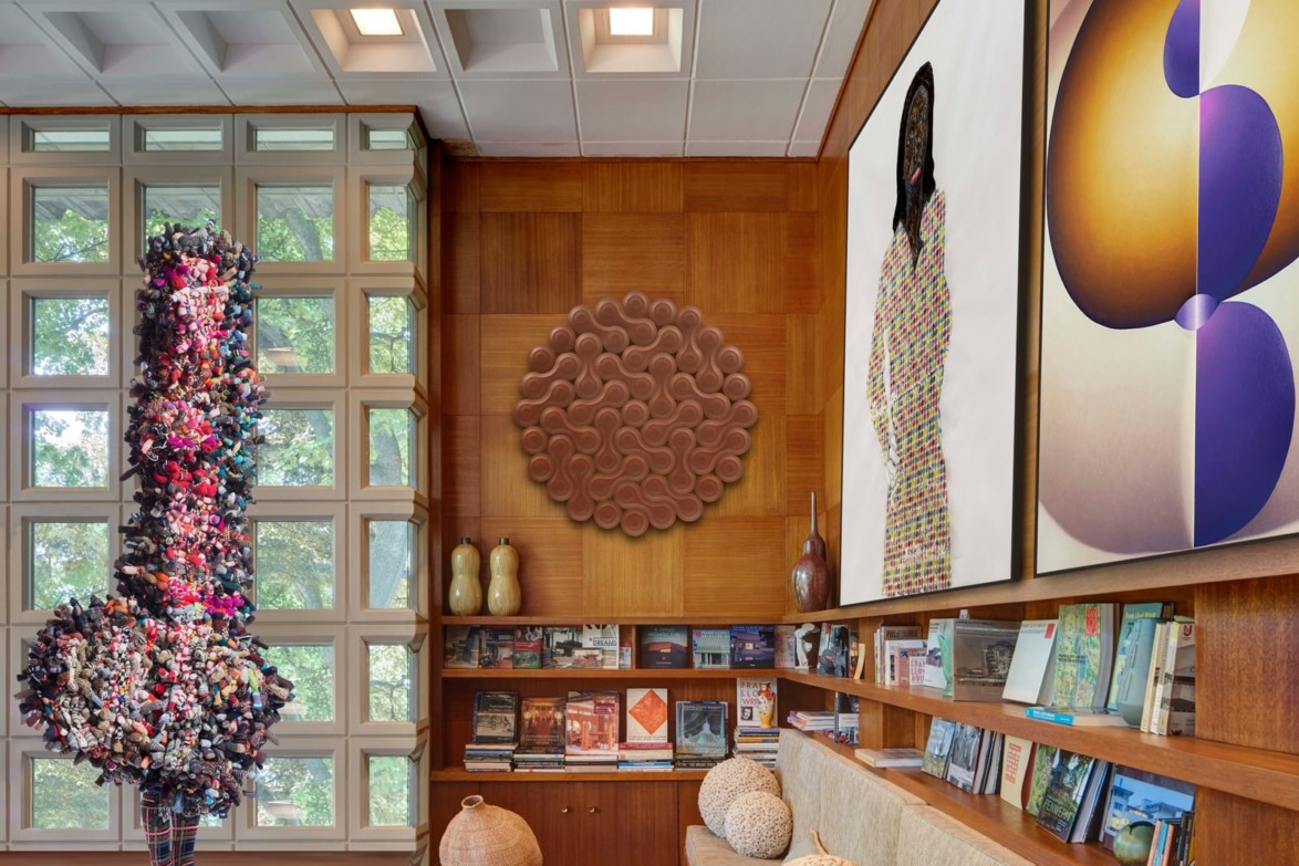 Art-filled room with wooden walls, a colorful sculpture, abstract paintings, and books on a shelf.