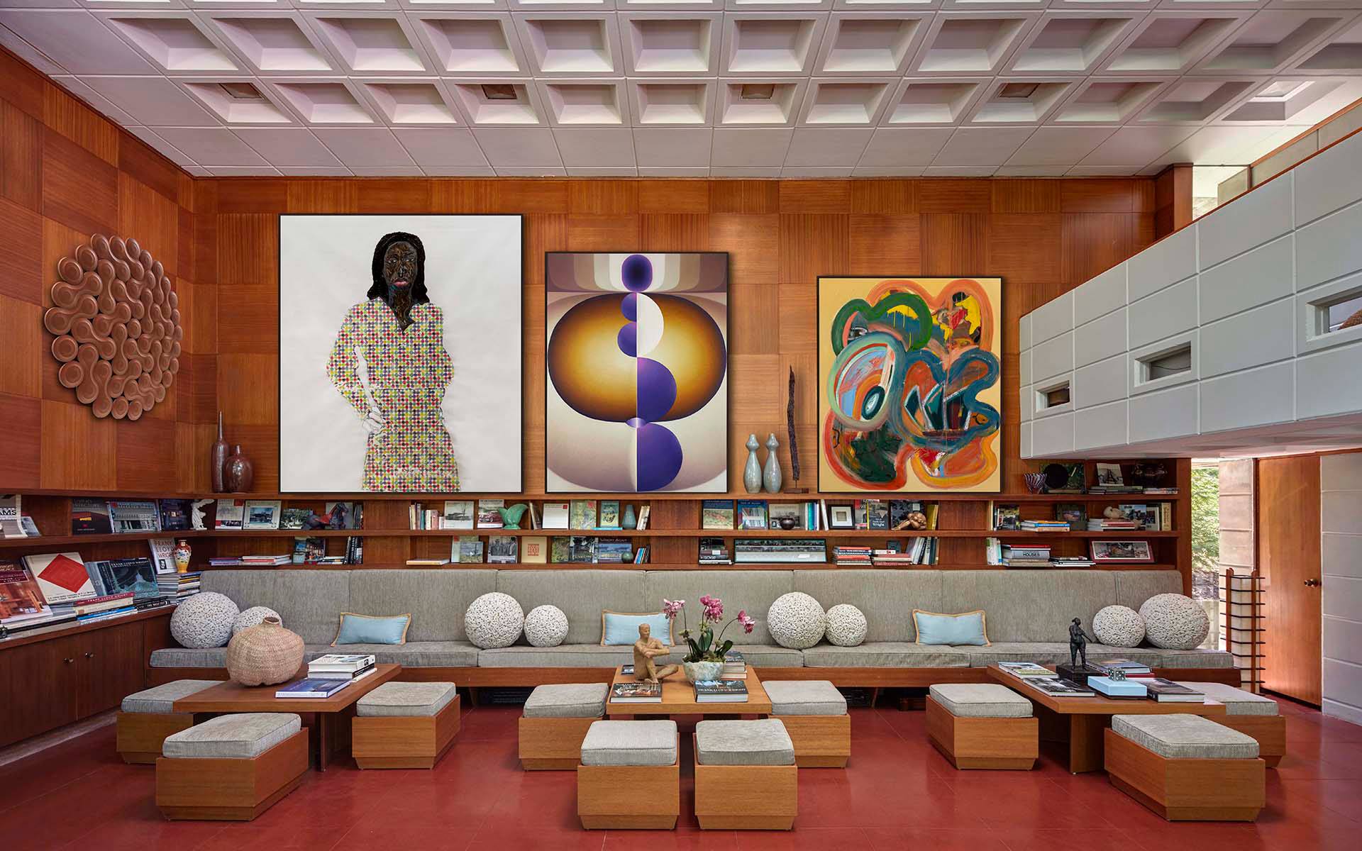 Cozy living room with colorful abstract art and sculptures, featuring wooden paneling and a long seating arrangement.