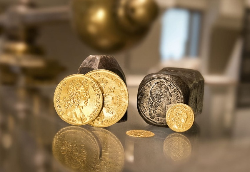 Golden and silver coins displayed on a reflective surface with blurred background.