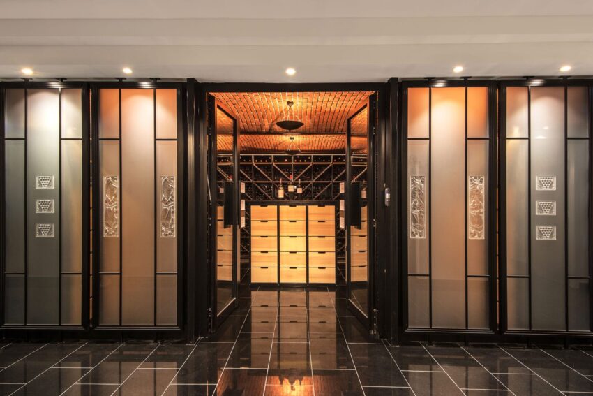 Modern wine cellar with glass doors, backlit shelving, and elegant lighting, featuring an extensive collection of wine bottles.