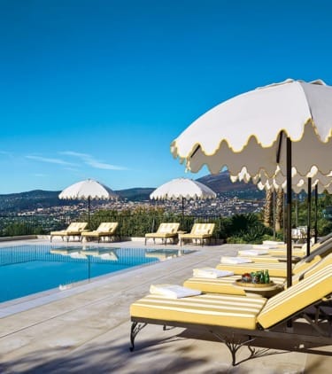 Poolside lounge chairs and umbrellas with scenic mountain view in the background.
