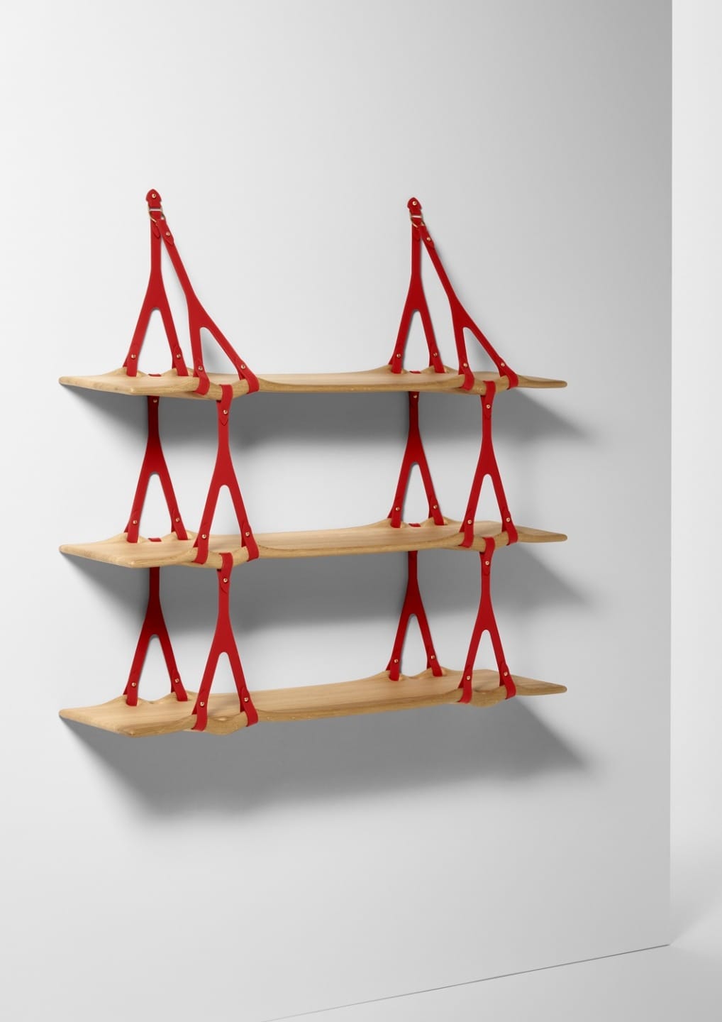 Wall-mounted shelves with red brackets and wooden planks, resembling a suspension bridge design, against a white wall.