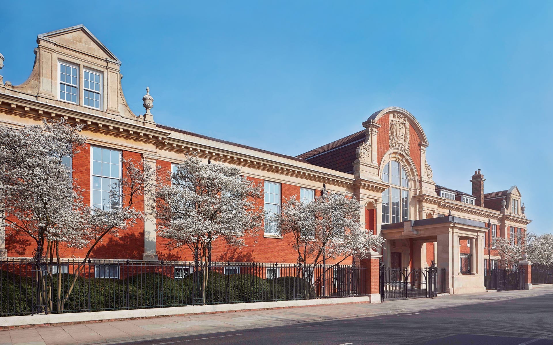 Red brick building with large arched windows, surrounded by blooming trees on a clear day.
