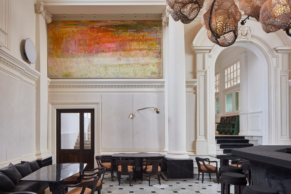 Elegant modern restaurant interior with tall columns, large abstract painting, black seating, and unique ceiling light fixtures.