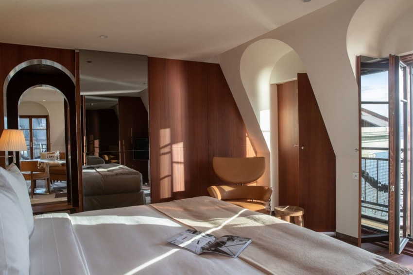 Modern hotel room with stylish wood paneling, bed, chair, and open balcony door letting in natural light.