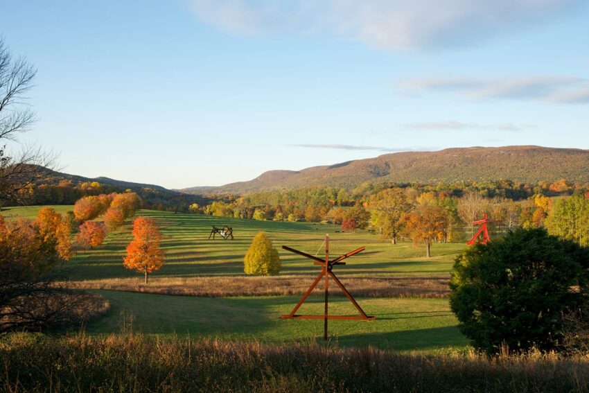 Scenic view of a grassy landscape with colorful autumn trees and large metal sculptures under a blue sky.