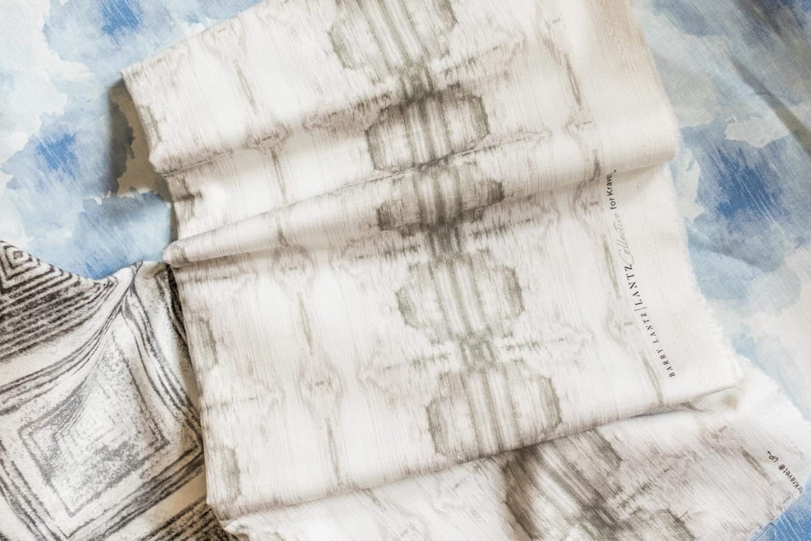 Textile samples with abstract patterns in shades of gray spread on a blue and white watercolor background.