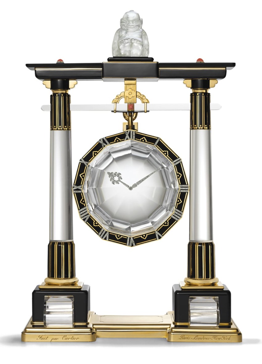 Art Deco pendulum clock with black and gold columns, crystal centerpiece, and ornate details, topped with a small sculpture.