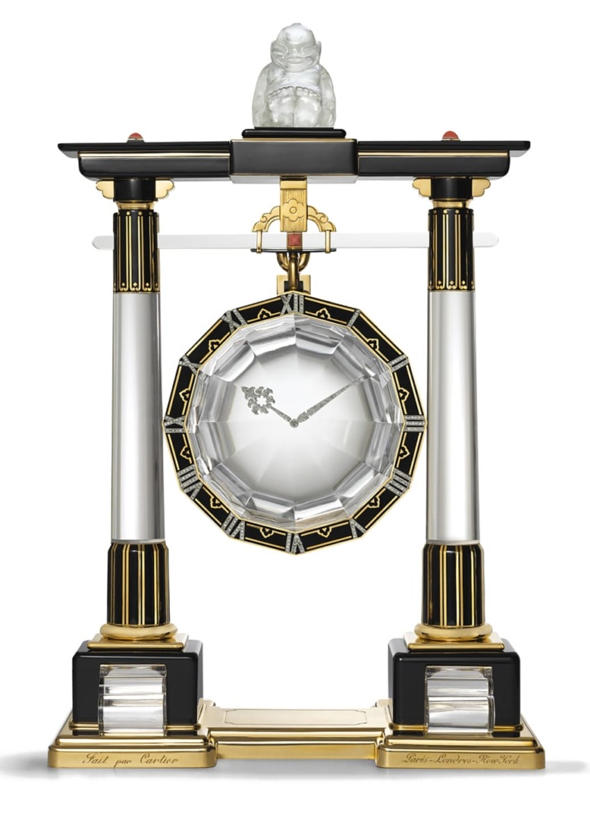 Art Deco pendulum clock with black and gold columns, crystal centerpiece, and ornate details, topped with a small sculpture.