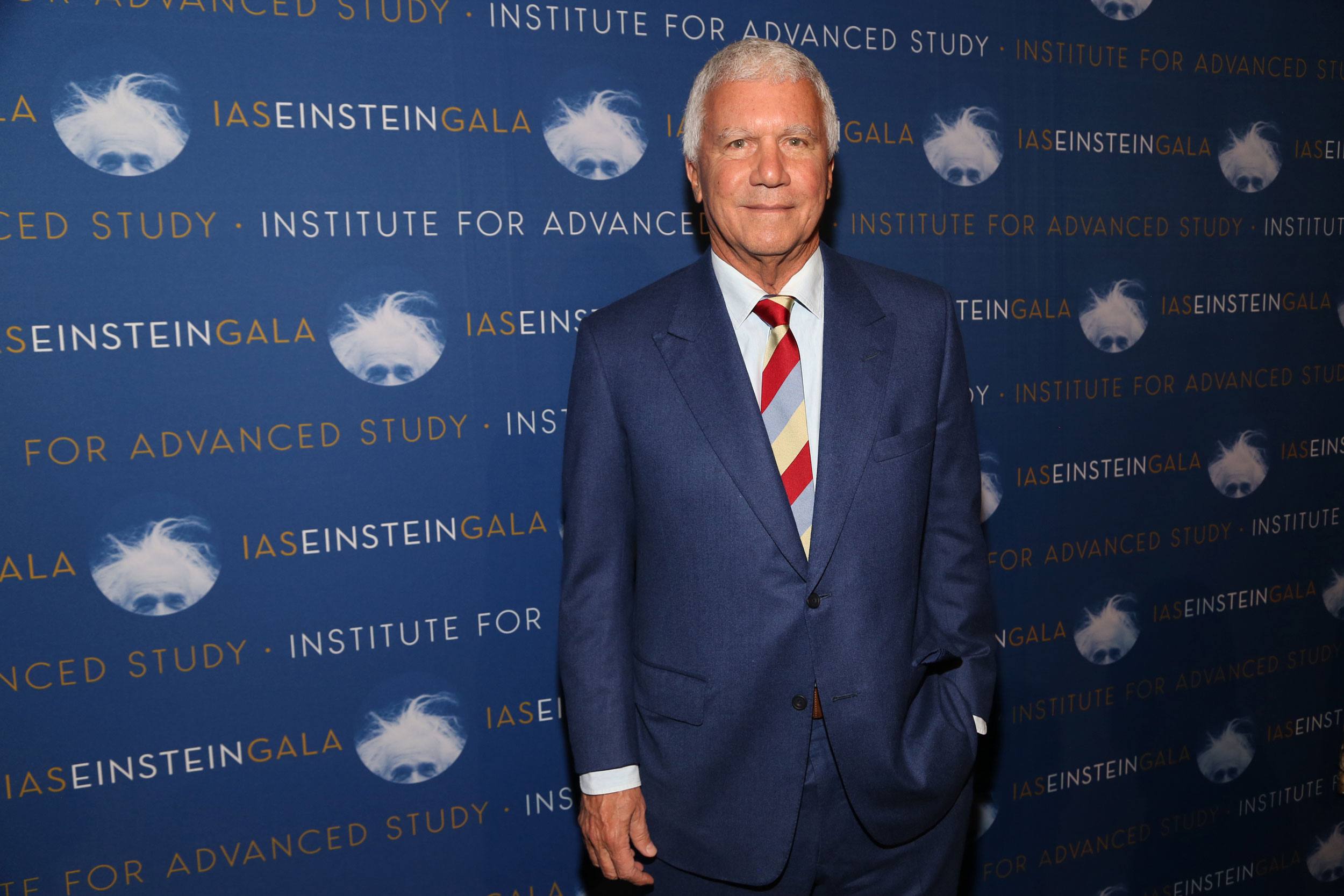 Man in a blue suit posing at the Institute for Advanced Study event against a branded backdrop.
