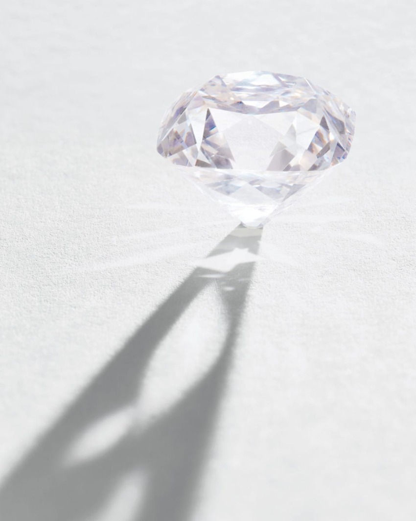 Faceted diamond casting shadow on a textured white surface in bright light.