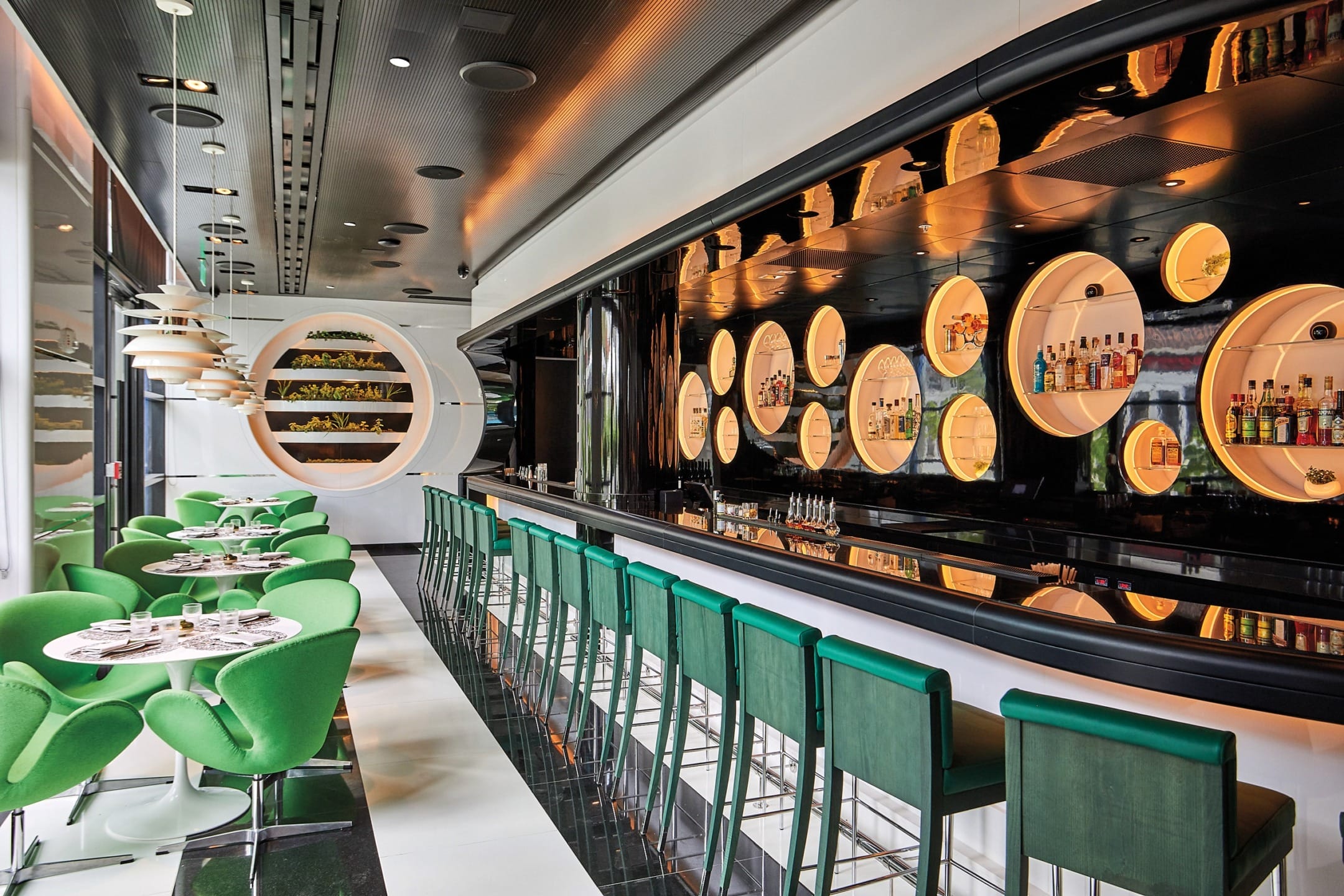 Modern bar and lounge with green chairs, circular shelves, and a sleek, contemporary design.