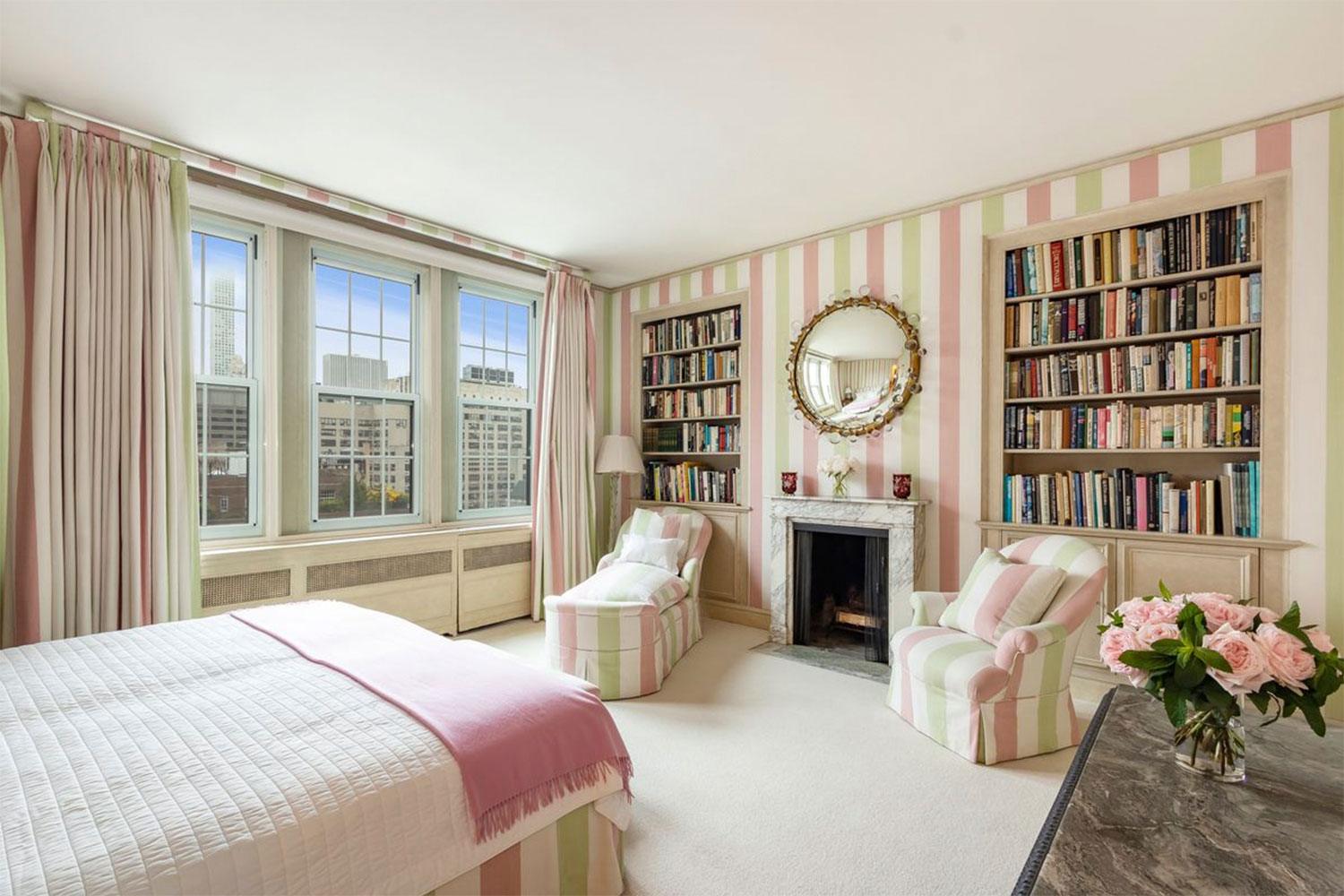 Elegant bedroom with striped pink-green wallpaper, large window, bookshelves, ornate mirror above fireplace, and cozy seating.
