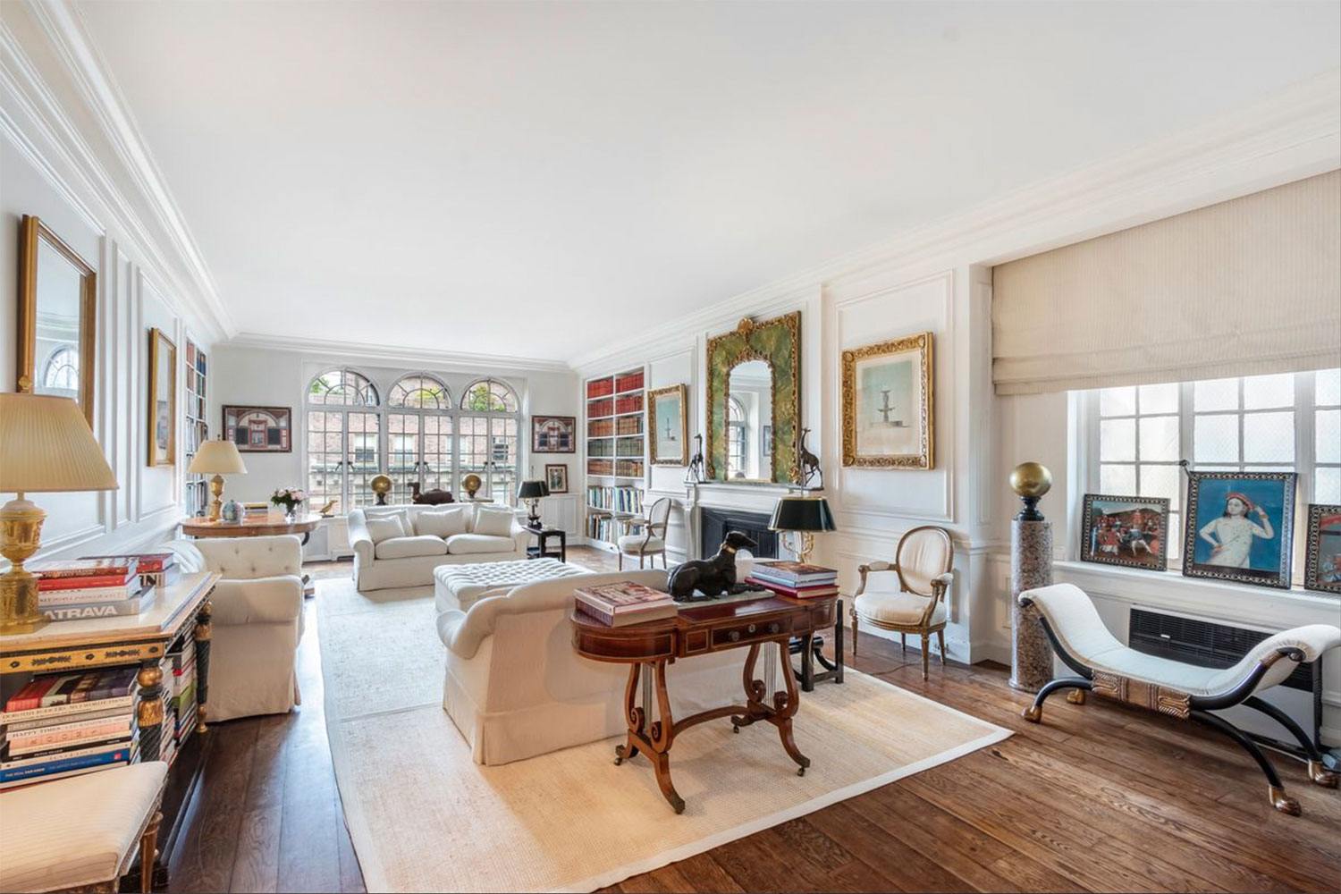 Elegant living room with vintage furniture, large windows, and a cozy fireplace surrounded by bookshelves and artwork.