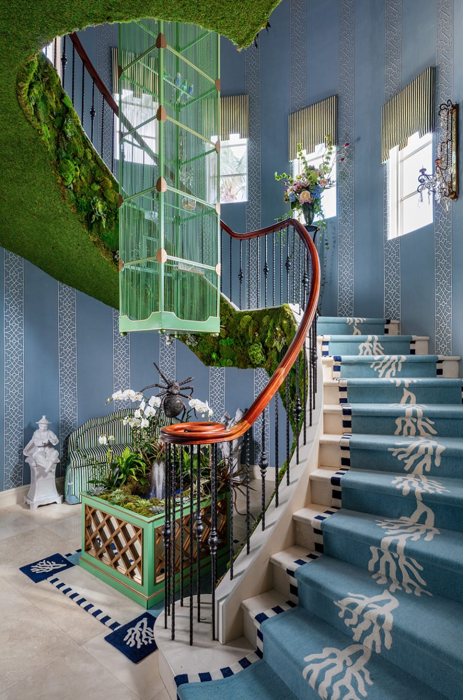 Spiral staircase with blue carpet, green moss-covered railing, and green birdcage in an elegantly decorated interior.