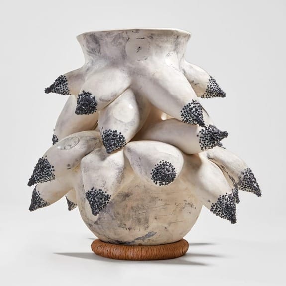 Unique sculptural vase with organic, spiky texture and ivory tones, placed on a round base against a plain background.