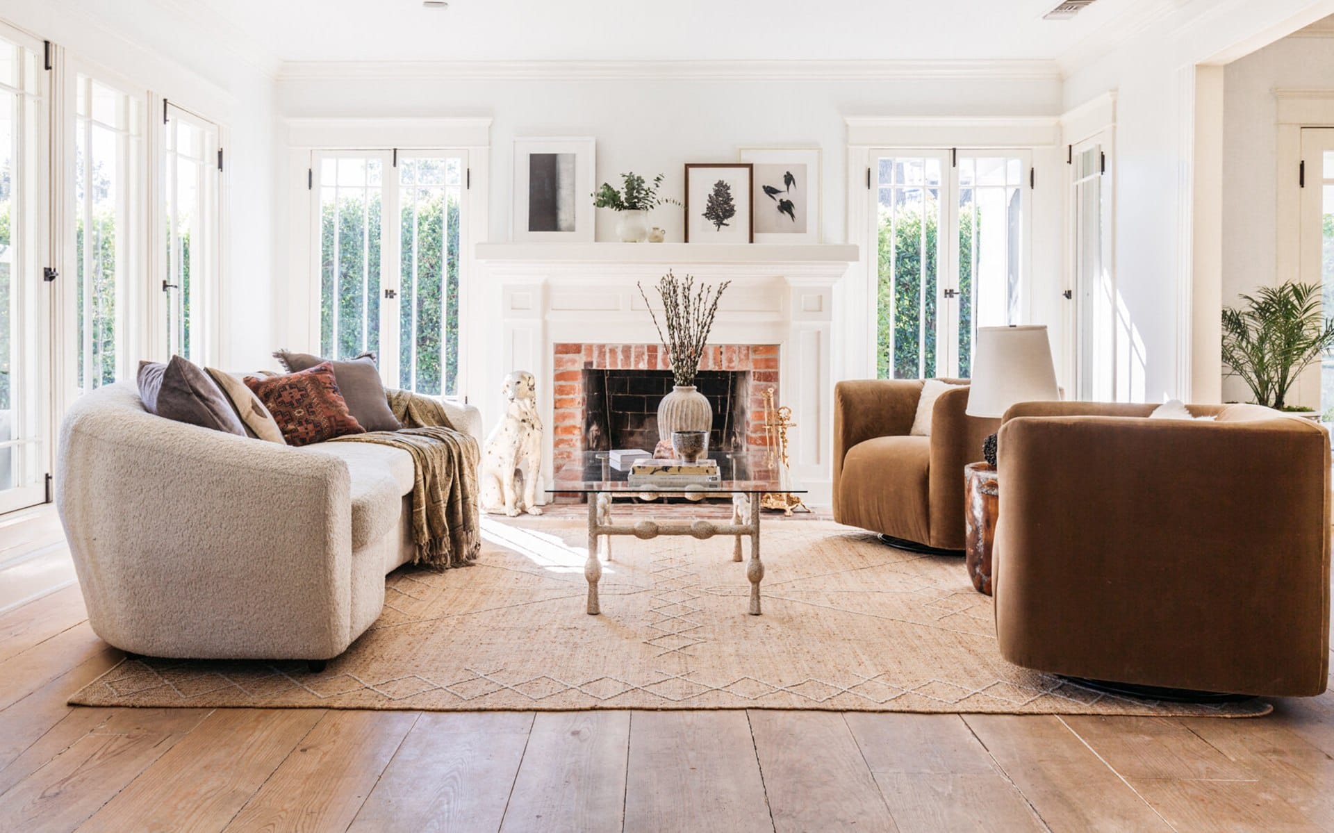 Bright living room with modern furniture, large windows, and a fireplace, featuring a cozy rug and decorative plants.